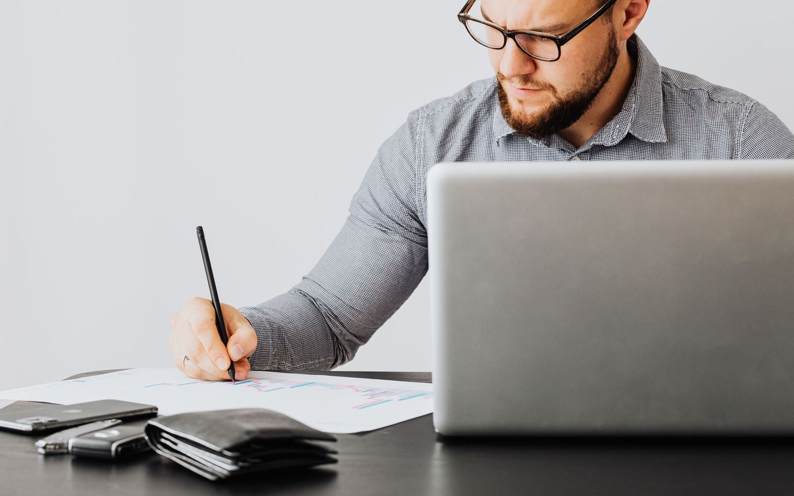 Une personne compare des documents posés à côté d'un ordinateur portable